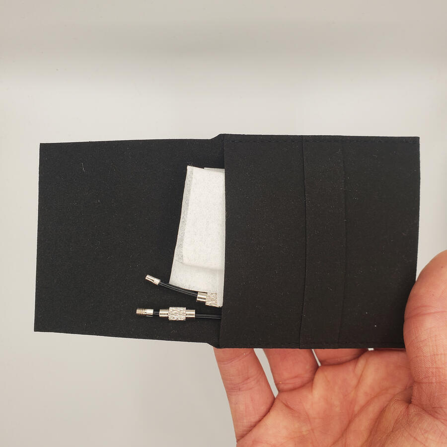 Untitled An open pouch with two wrapped-up anodized aluminum laser-engraved. Two opened key chain keyloops are also tucked in the pouch.